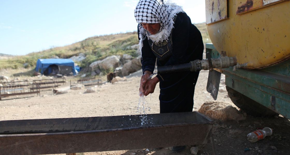 Eine ältere Frau wäscht sich die Hände mit Wasser aus einem großen Tank auf Rädern