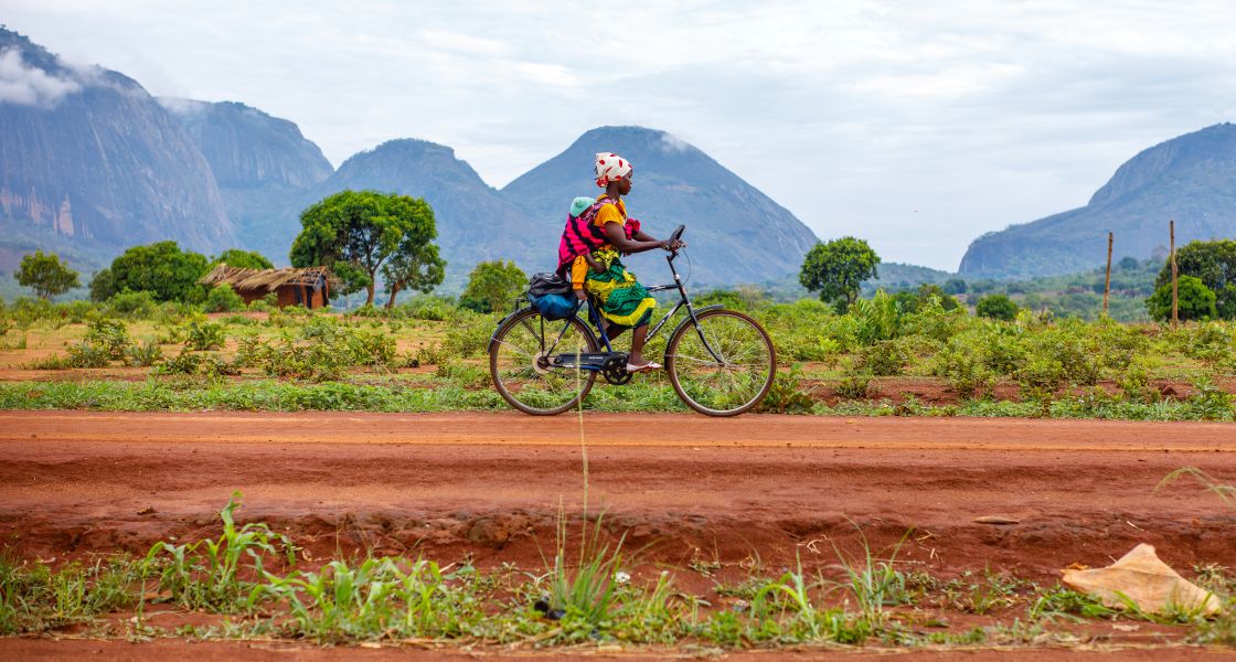 eine Frau mit Kind fährt Fahrrad auf einer Straße in Nampula