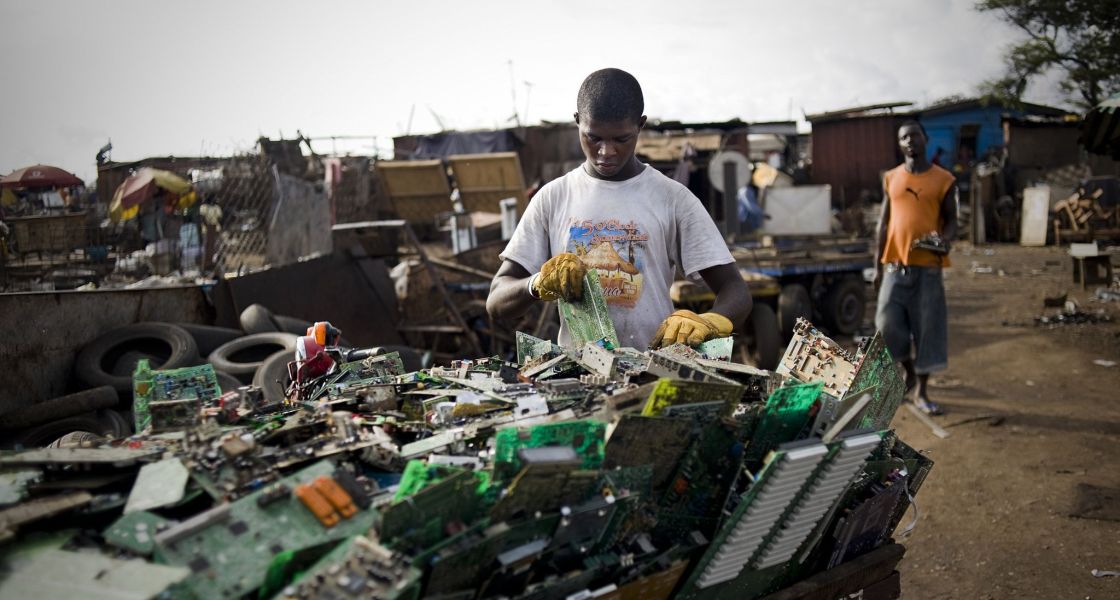 Schwarzer Mann sortiert Platinen und anderen Elektroschrott in einem Container