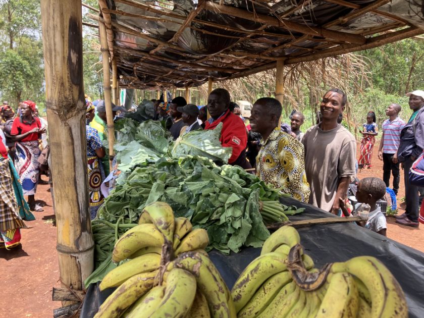 Eine Gruppe Männer und Frauen verkaufen ihr Gemüse an überdachten Ständen.