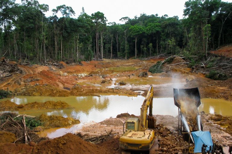 Ein Bagger und eine Maschinen stehen an einem Tümpel mitten in einer entholzten Fläche im Tropenwald