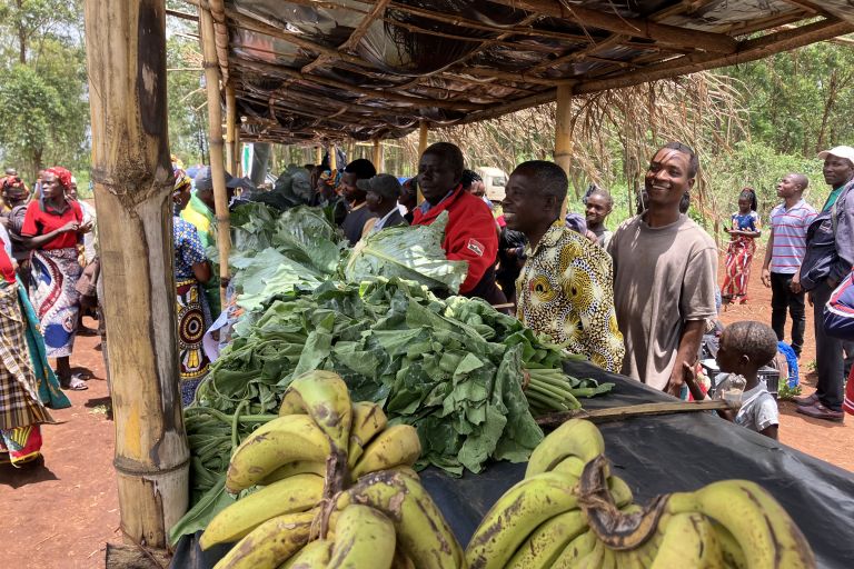 Eine Gruppe Männer und Frauen verkaufen ihr Gemüse an überdachten Ständen.